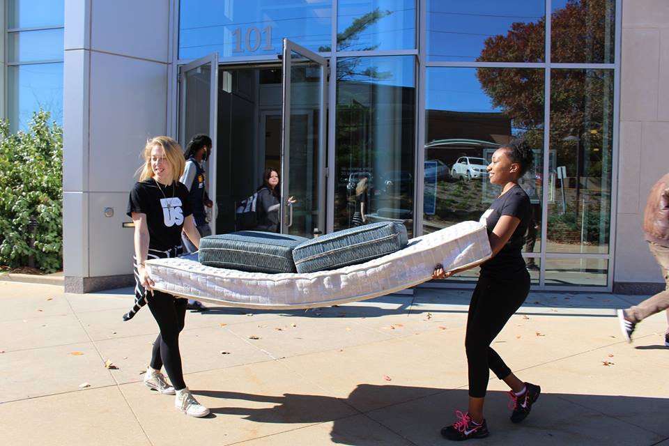 Two people carrying a mattress outdoors