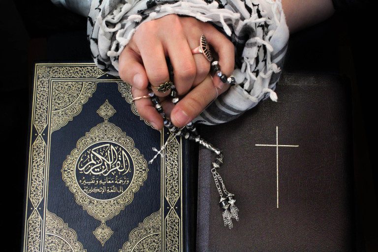 Hands holding rosary over Quran and Bible