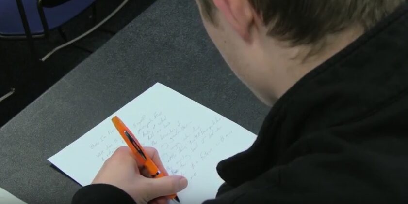 Student writing with orange pen