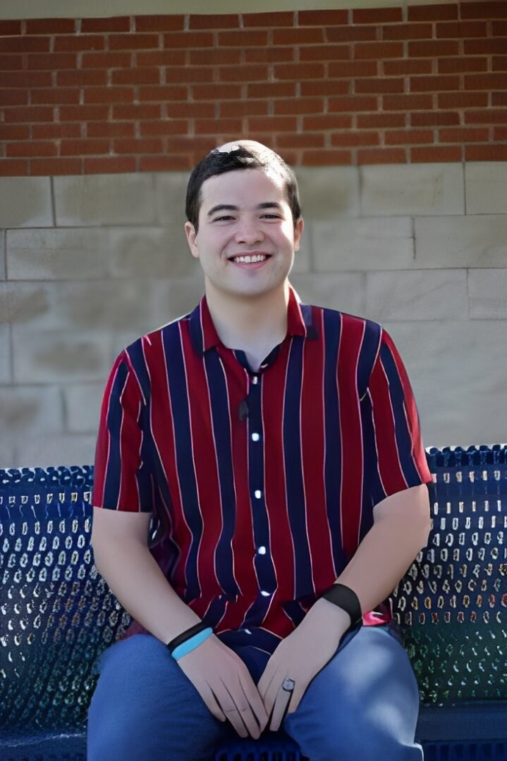 Happy individual seated against a brick wall.