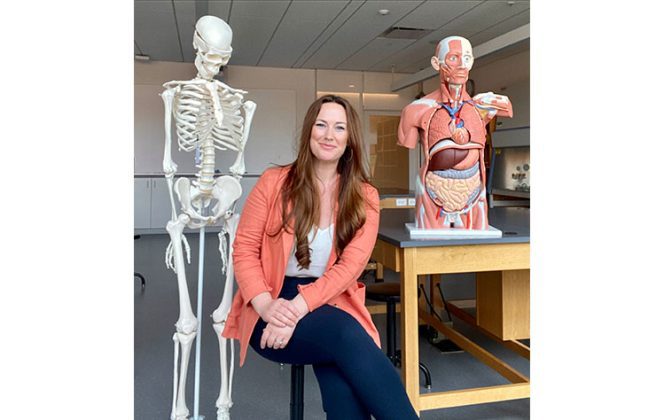 Smiling woman between skeleton and torso model