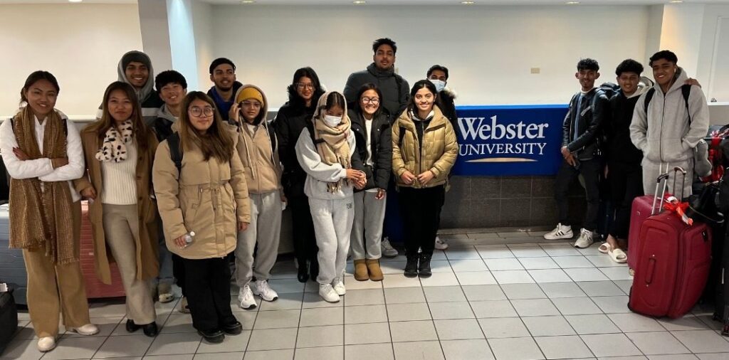 Students posing indoors with luggage.