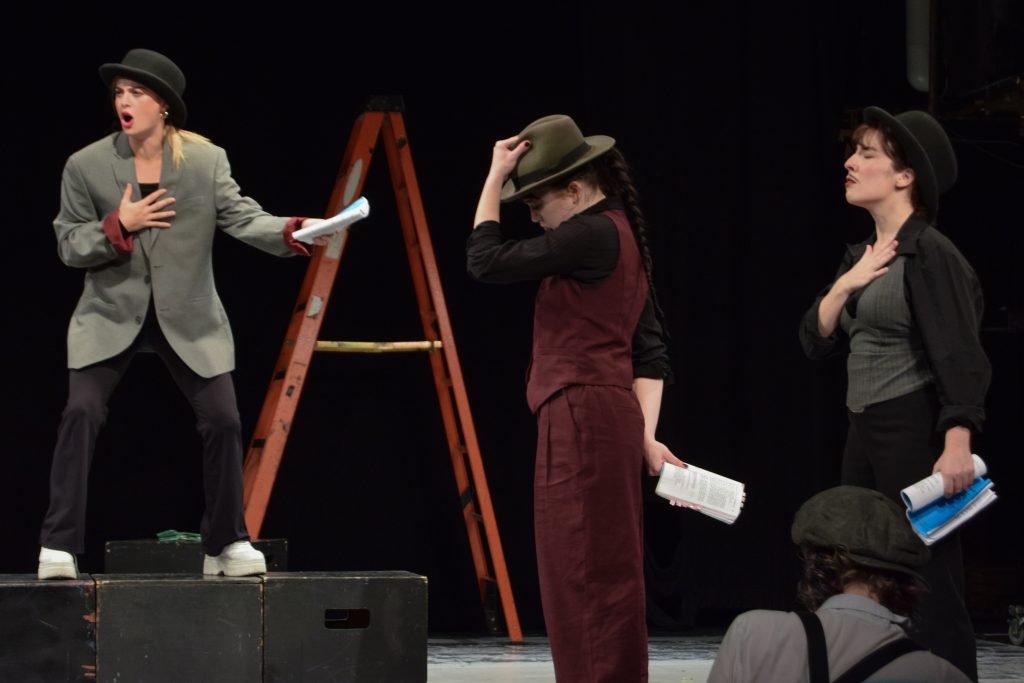 Three actors in hats rehearsing play