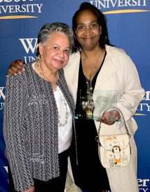 Two smiling women posing with award, university backdrop