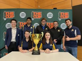 Team posing with trophy in front of banner
