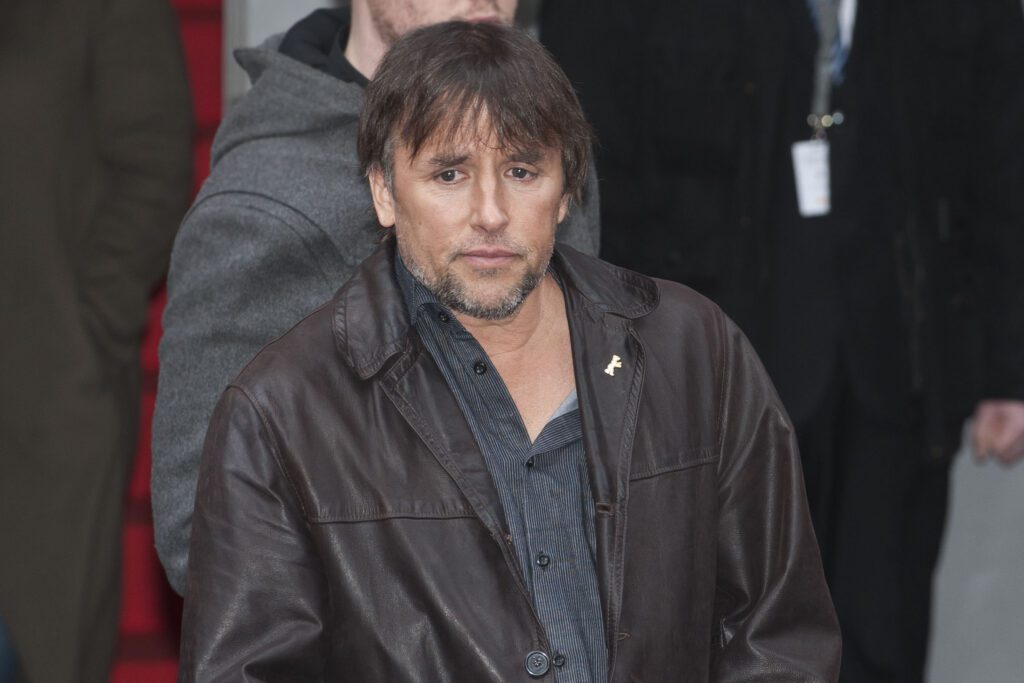 Individual standing, wearing a button-up shirt