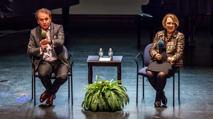 Two people seated on stage with microphones.