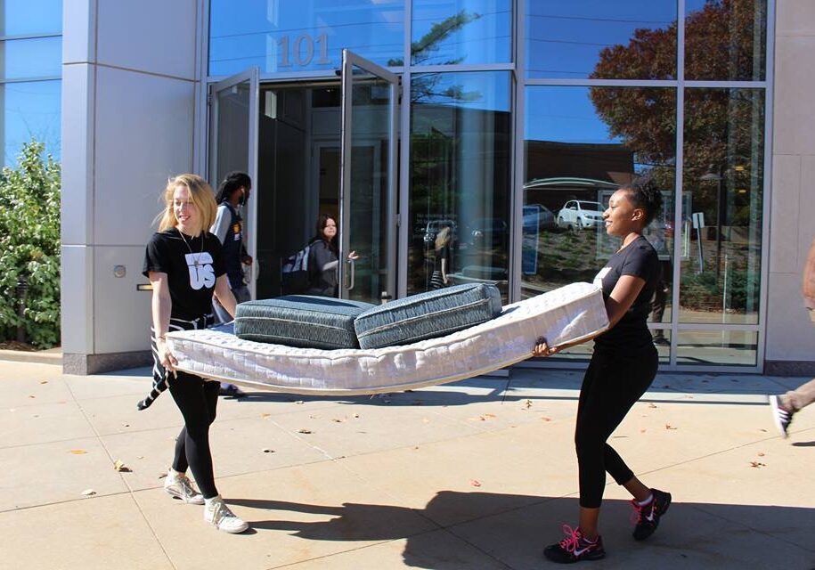 Two people carrying a mattress outdoors