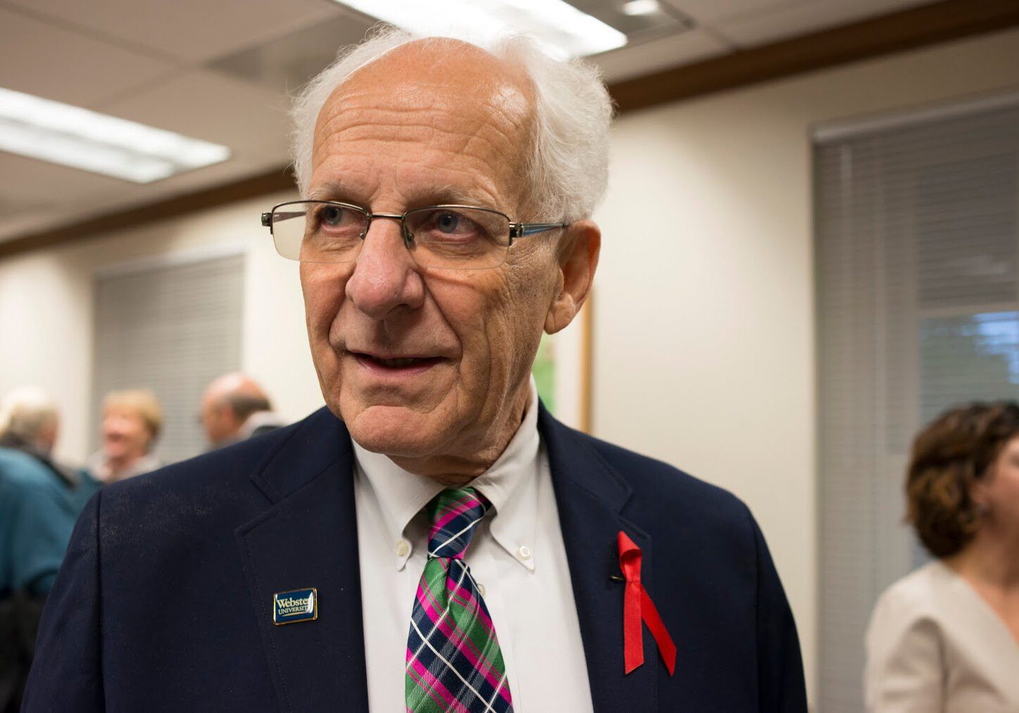 Elderly man in suit with red ribbon