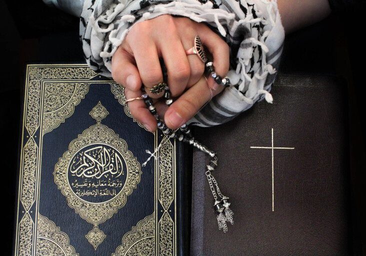 Hands holding rosary over Quran and Bible