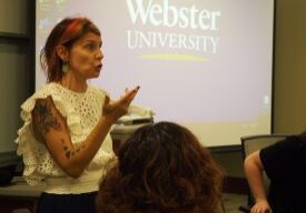 Instructor speaking before Webster University projected logo