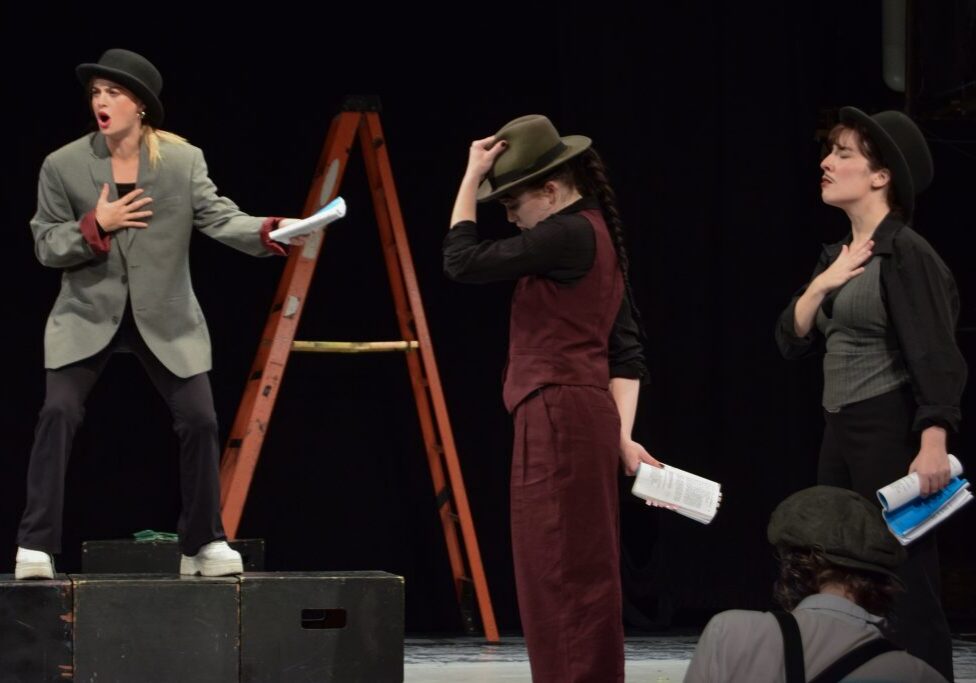 Three actors in hats rehearsing play