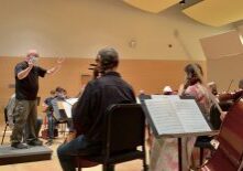 Conductor leading orchestra rehearsal in concert hall