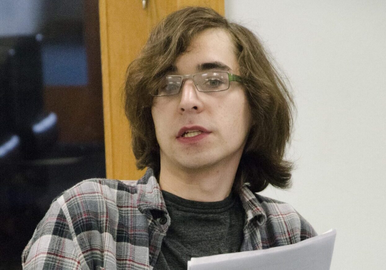 Individual with glasses, long hair, reading