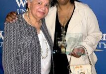 Two smiling women posing with award, university backdrop
