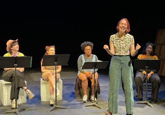 Woman speaking on stage with seated audience.