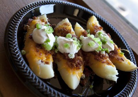 Potato skins with toppings on black plate.