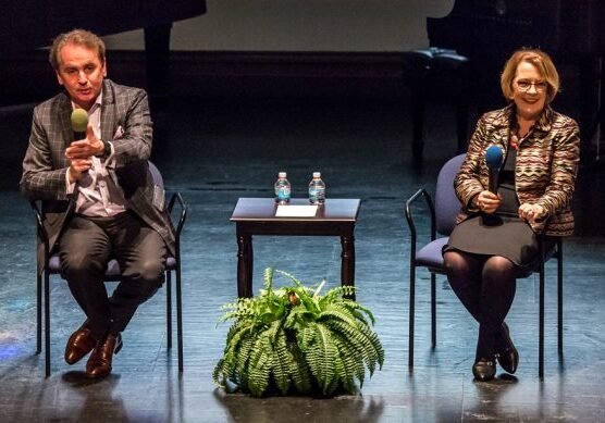 Two people seated on stage with microphones.
