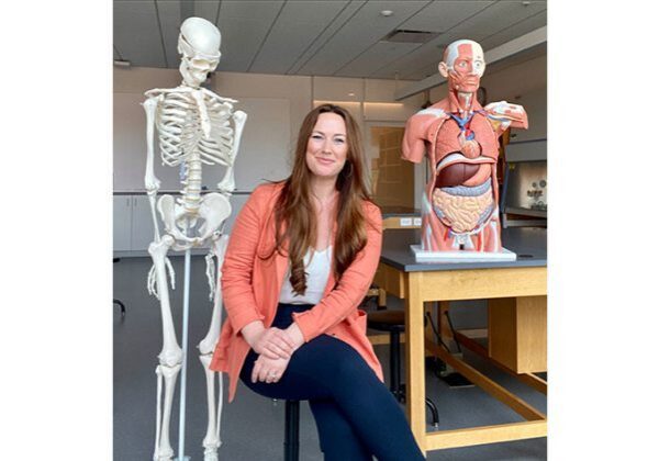 Smiling woman between skeleton and torso model