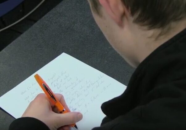 Student writing with orange pen